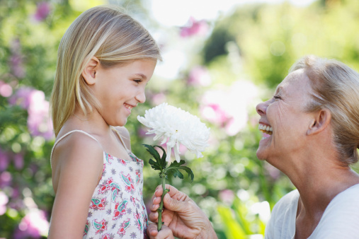 Grandmother giving flower to granddaughter in garden